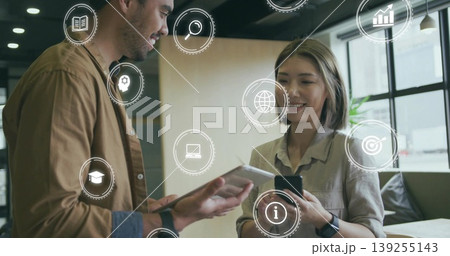 Discussing colleagues reviewing digital icons in office lounge by windows, with tablet smartphone 139255143