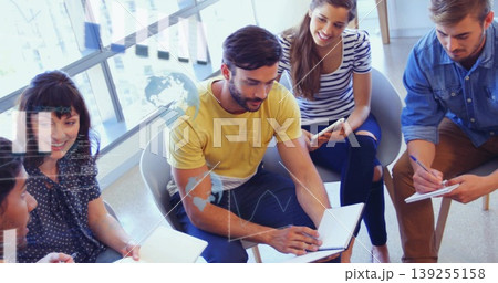 Holding notebooks, tablets and pens, colleagues brainstorming at low table in lounge by windows Holding notebooks, tablets and pens, colleagues brainstorming at low table in lounge by windows 139255158