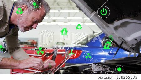 Inspecting senior male mechanic leaning over engine bay at workshop, with laptop and energy icons Inspecting senior male mechanic leaning over engine bay at workshop, with laptop and energy icons 139255333