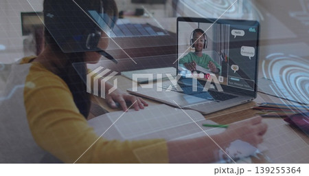 Sitting girl wearing headset writing notebook at home, with laptop showing classmate, pencils 139255364