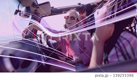 Laughing woman wearing sunglasses and pink top driving red convertible on road, with neon streaks Laughing woman wearing sunglasses and pink top driving red convertible on road, with neon streaks 139255398