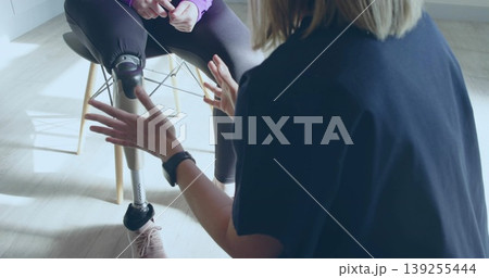 Clinician kneeling adjusting patient's below-knee prosthetic leg in therapy clinic, with smartwatch 139255444