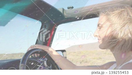 Driving woman gripping steering wheel across bright arid road, revealing open top frame, copy space 139255453