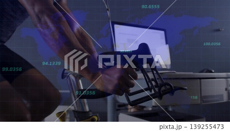 Pedaling cyclist gripping aero handlebars in office workstation, world map and metrics overlaying Pedaling cyclist gripping aero handlebars in office workstation, world map and metrics overlaying 139255473