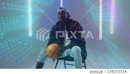 Sitting adult male holding basketball in hazy studio, with LED tubes, holographic dots Sitting adult male holding basketball in hazy studio, with LED tubes, holographic dots 139255554