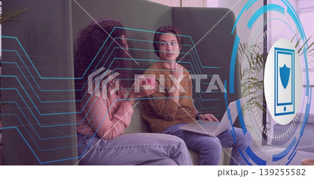 Two colleagues analyzing circuit and shield overlays on green lounge sofa with red mug and laptop Two colleagues analyzing circuit and shield overlays on green lounge sofa with red mug and laptop 139255582
