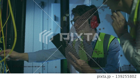 Male engineer with vest holding clipboard in data center rack, colleague adjusting patch cables 139255802