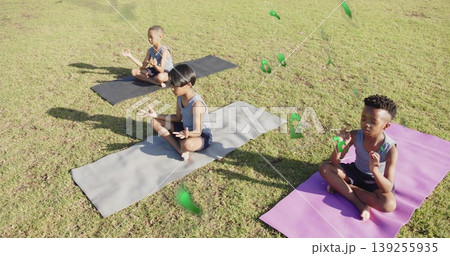 Meditating three boys in sleeveless tops, shorts on yoga mats in park, with floating green shapes Meditating three boys in sleeveless tops, shorts on yoga mats in park, with floating green shapes 139255935