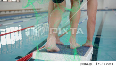Standing swimmers wearing swimwear balancing on starting block at pool with red lane divider ropes 139255964