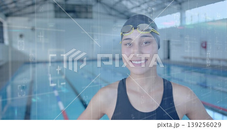 Standing swimmer wearing racing swimsuit, swim cap and goggles at competition pool, with lane lines Standing swimmer wearing racing swimsuit, swim cap and goggles at competition pool, with lane lines 139256029