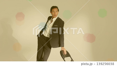 Leaning model wearing black suit and white shirt gazing left in pastel studio, with folding chair Leaning model wearing black suit and white shirt gazing left in pastel studio, with folding chair 139256038