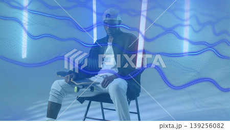 Holding skateboard skateboarder sitting on stool in studio, with neon tubes and blue wave trails 139256082