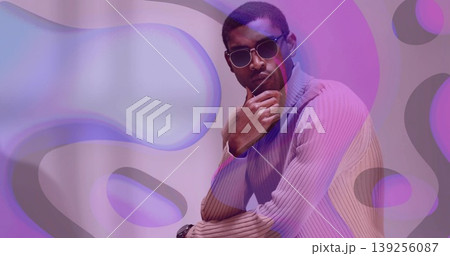 Posing man touching chin wearing turtleneck and sunglasses in studio, abstract backdrop Posing man touching chin wearing turtleneck and sunglasses in studio, abstract backdrop 139256087