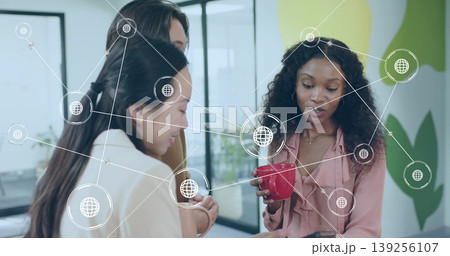 Leaning three business casual colleagues viewing smartphone at office space, with red coffee mug Leaning three business casual colleagues viewing smartphone at office space, with red coffee mug 139256107