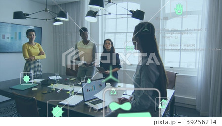 Gesturing presenter and colleagues reviewing reports around meeting table in office, with laptops 139256214