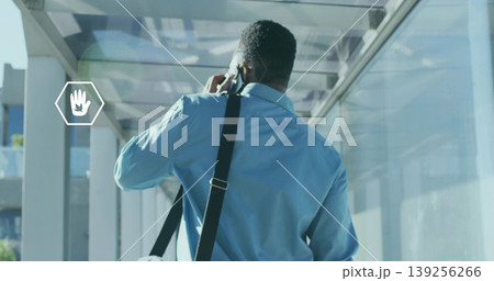 Talking man wearing light blue shirt holding smartphone to ear in glass corridor, messenger bag Talking man wearing light blue shirt holding smartphone to ear in glass corridor, messenger bag 139256266
