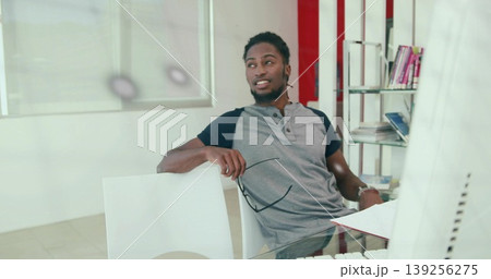 Leaning man holding glasses, looking off to side at glass desk in office, with monitor, books Leaning man holding glasses, looking off to side at glass desk in office, with monitor, books 139256275
