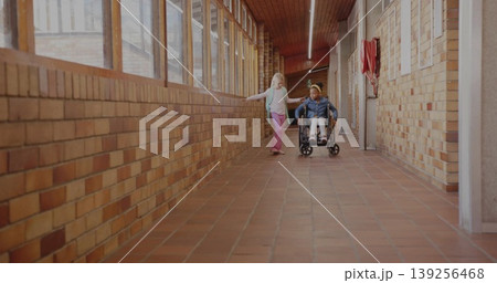 Two classmates rolling wheelchair and walking with backpack in school hall, with fire hose cabinet Two classmates rolling wheelchair and walking with backpack in school hall, with fire hose cabinet 139256468
