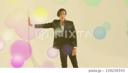 Posing Asian model extending left arm on white vertical panel in cream studio, with pastel circles Posing Asian model extending left arm on white vertical panel in cream studio, with pastel circles 139256543