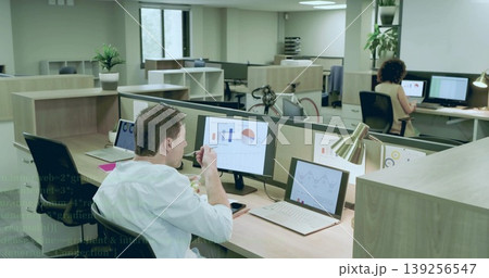 Office worker eating snack bowl in open-plan office, reviewing charts on dual monitors, copy space 139256547