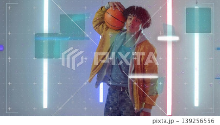 Cradling basketball model posing on studio set with neon fluorescent tubes and square grid overlays 139256556