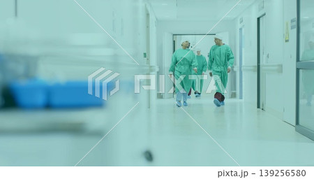 Walking surgical team wearing scrubs and shoe covers along hospital corridor, with trolley 139256580
