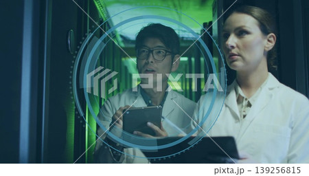 Two IT technicians projecting and analyzing 3D interface in hall, with server racks and tablets 139256815