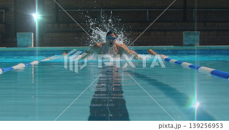Swimming man performing butterfly stroke at enclosed pool, with swim cap, goggles and lane dividers 139256953