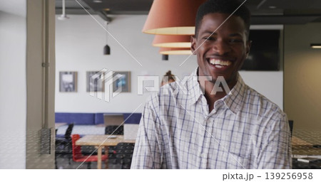 Smiling checkered shirt man standing in office with furniture, lamps, photos, monitor, copy space 139256958