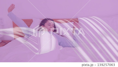 Stretching Indian woman wearing blue pajamas in bedroom with bed duvet pillows nightstand lamp 139257063