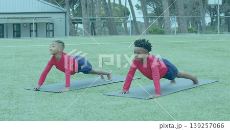 Holding plank pose two boys wearing red shirts and navy shorts on grass field, with mats 139257066