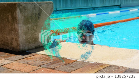 Swimmer wearing cap holding pool edge at outdoor pool wall, with starting block and lane divider 139257235