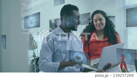 Two colleagues in button-up shirts collaborating in office, reviewing laptop with digital overlays Two colleagues in button-up shirts collaborating in office, reviewing laptop with digital overlays 139257269