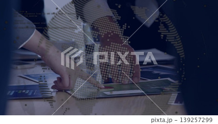 Pointing hands analyzing printed charts at office desk, with digital globe, code text overlay 139257299