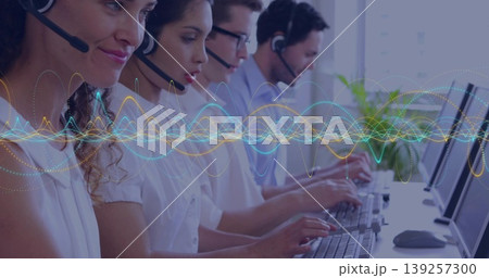 Typing call center agents wearing headsets at office desk, with keyboards, wave graphic overlay Typing call center agents wearing headsets at office desk, with keyboards, wave graphic overlay 139257300
