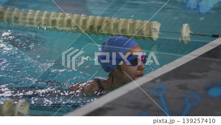 Swimmer gripping pool edge near floating lane rope at lap pool, with blue swim cap, goggles Swimmer gripping pool edge near floating lane rope at lap pool, with blue swim cap, goggles 139257410