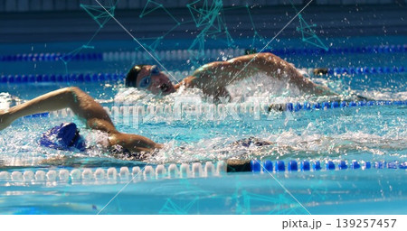 Two swimmers wearing caps and goggles racing in sports pool, with splashing water and divider ropes Two swimmers wearing caps and goggles racing in sports pool, with splashing water and divider ropes 139257457
