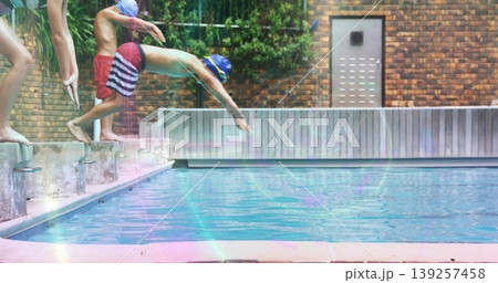 Diving boy in striped trunks and yellow swim cap arcing over pool edge, with starting blocks Diving boy in striped trunks and yellow swim cap arcing over pool edge, with starting blocks 139257458