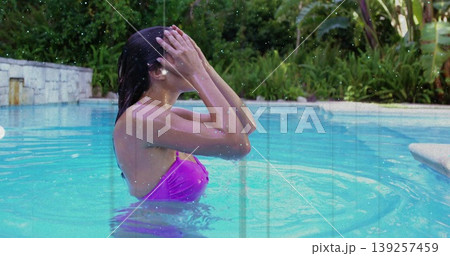 Woman lifting hair away from face, standing in pool with water surface, tropical plants, copy space Woman lifting hair away from face, standing in pool with water surface, tropical plants, copy space 139257459