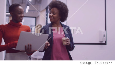 Walking coworkers in formal attire through office hallway, pointing at laptop, holding coffee cup 139257577