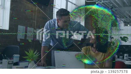Leaning man in blue shirt and woman in yellow blouse collaborating at open-plan office, with laptop 139257578