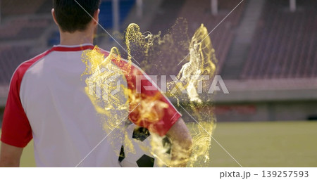 Standing male soccer player holding ball on grass pitch, with golden particle effect, copy space Standing male soccer player holding ball on grass pitch, with golden particle effect, copy space 139257593