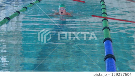 Gliding swimmer wearing green swim cap white swim goggles through lap pool, with colored lane ropes Gliding swimmer wearing green swim cap white swim goggles through lap pool, with colored lane ropes 139257604