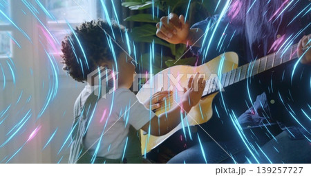 Holding acoustic guitar mother in shirt guiding son reaching strings in living room with neon light Holding acoustic guitar mother in shirt guiding son reaching strings in living room with neon light 139257727
