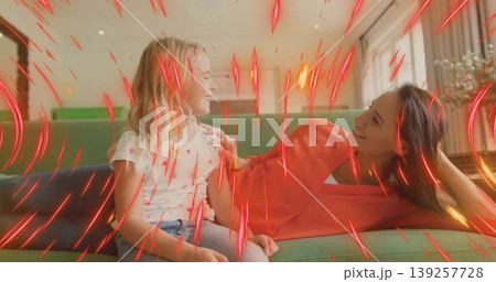 Mother in red dress and daughter sharing smiles on green sofa in living room with plant 139257728