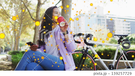 Asian woman holding red coffee cup to lips, checking smartphone on park bench with road bicycle 139257729