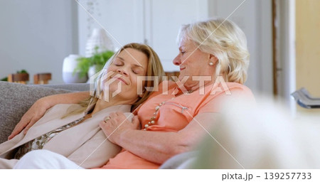 Relaxing adult daughter leaning on mother's shoulder in living room, with gray couch, vases, plants 139257733