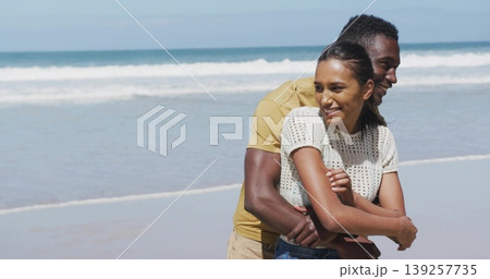 Hugging couple wearing casual summer clothes on sandy beach at water's edge, with ocean waves 139257735