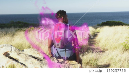 Sitting male hiker facing sea horizon on coastal bluff, with red-gray daypack and purple mist 139257736