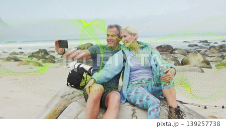 Posing hikers capturing selfie on driftwood log by rocky beach, with smartphone, backpack and poles 139257738